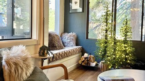 Un salon chaleureux avec un canapé, une petite table, un sapin de Noël et une fenêtre donnant sur les arbres.