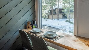 Une table à manger avec des assiettes, un verre à vin et une guitare, le tout placé devant une fenêtre donnant sur un paysage enneigé.