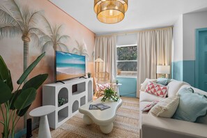 A living room with a TV, a white sofa, a coffee table, and a painting of palm trees. - Stylish 5min Downtown Orlando (Orlando)