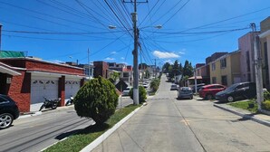 A residential street with houses, parked cars, and utility poles. - Casa Nimajay (Guatemala City)
