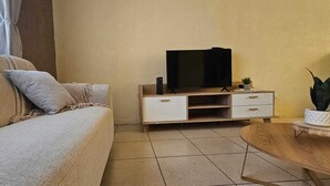 A living room with a sofa, a television on a wooden stand, a small table with a plant, and a window with curtains. - Casa Nimajay (Guatemala City)