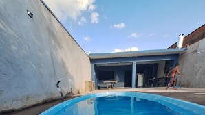 Une piscine avec une plage en béton, un bâtiment doté d’un garage et un ciel dégagé.