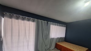 Une pièce avec un lit, des rideaux et un luminaire au plafond.