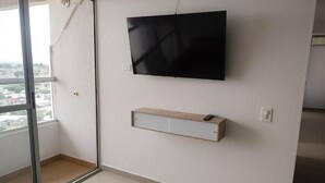 Une pièce dotée d’une grande fenêtre, d’un téléviseur à écran plat fixé au mur et d’une étagère en bois située en dessous.