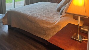 Una camera da letto con un letto, un comodino con una lampada, una cassettiera, uno specchio e una porta scorrevole in vetro che dà su un balcone.