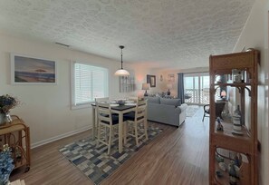 A dining area with a table and chairs, a sofa, a lamp, and a wall with a framed picture. - Maritime Place A5 - Oceanfront in Garden City Beach (Garden City Beach)