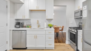 Une cuisine moderne avec des meubles blancs, un lave-vaisselle, une cuisinière et un four à micro-ondes.