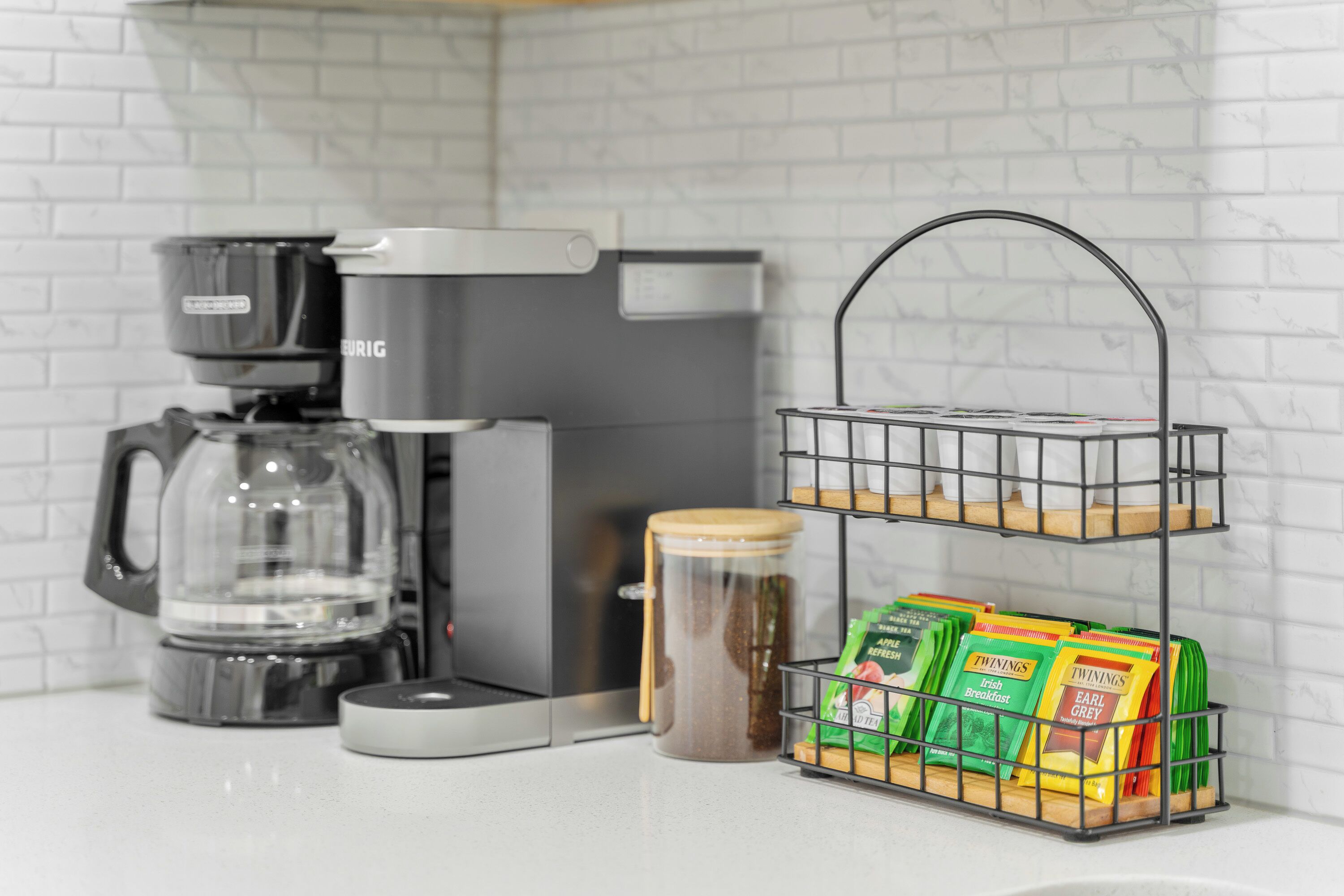 A kitchen with a coffee maker, a glass jar, and a wire basket holding packaged snacks.