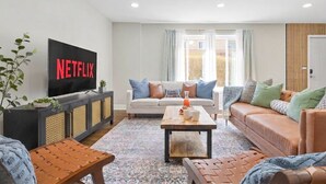 Un salon avec un téléviseur, des canapés, une table basse et une fenêtre avec des rideaux.