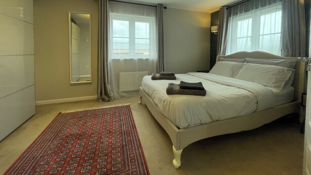 A bedroom with a bed, a mirror, a radiator, a window with curtains, and a patterned rug. - Entire Home. 3 bedroom house in Edinburgh suburb (Edinburgh)