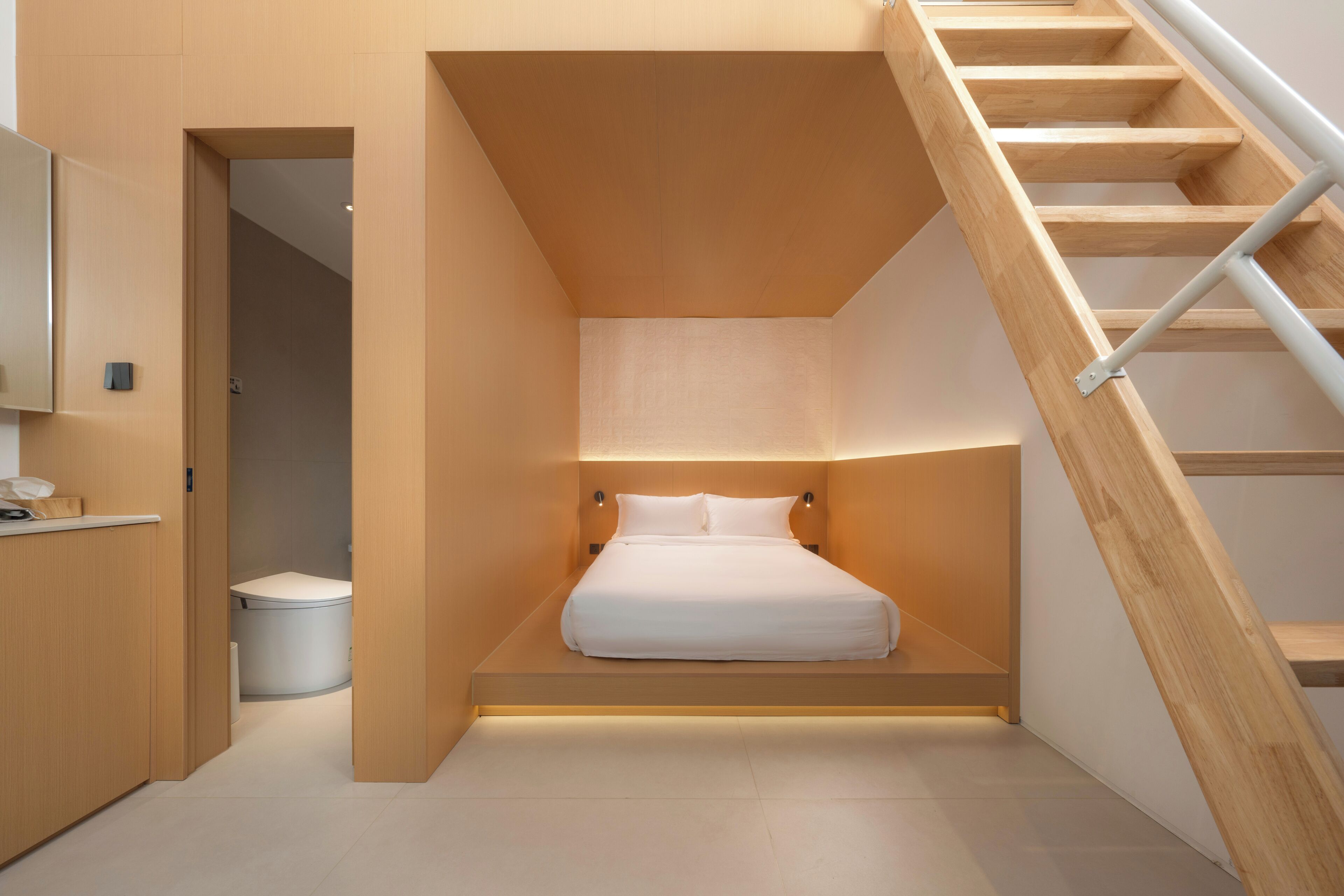 A modern bedroom with a built-in bed, a wooden staircase, and a small bathroom.