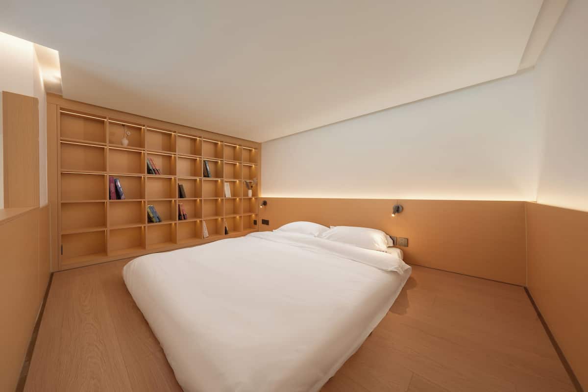 A bedroom with a large bed, wooden shelving unit, and a wall-mounted light.