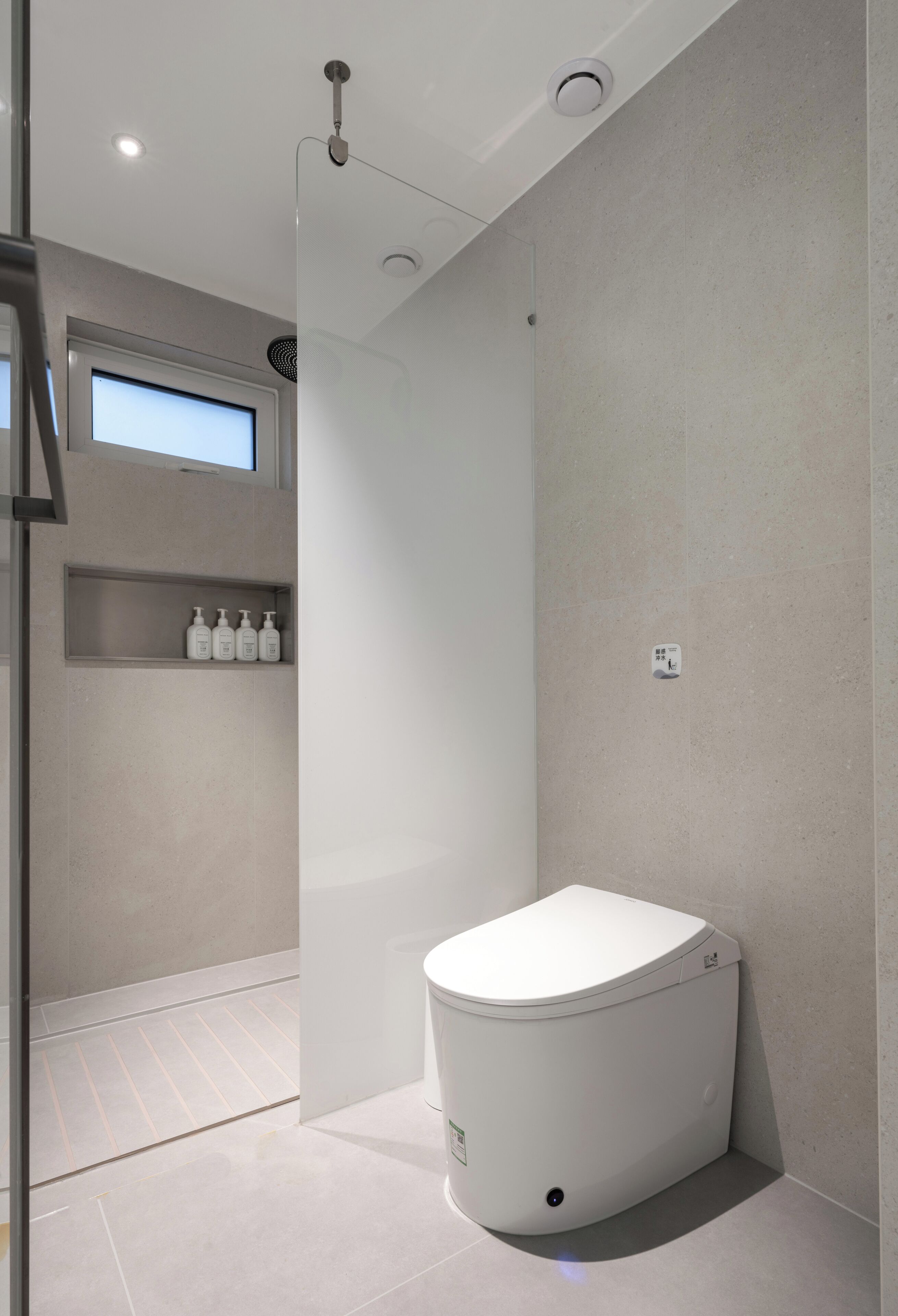A modern bathroom with a toilet, a shower area, and a shelf with toiletries.