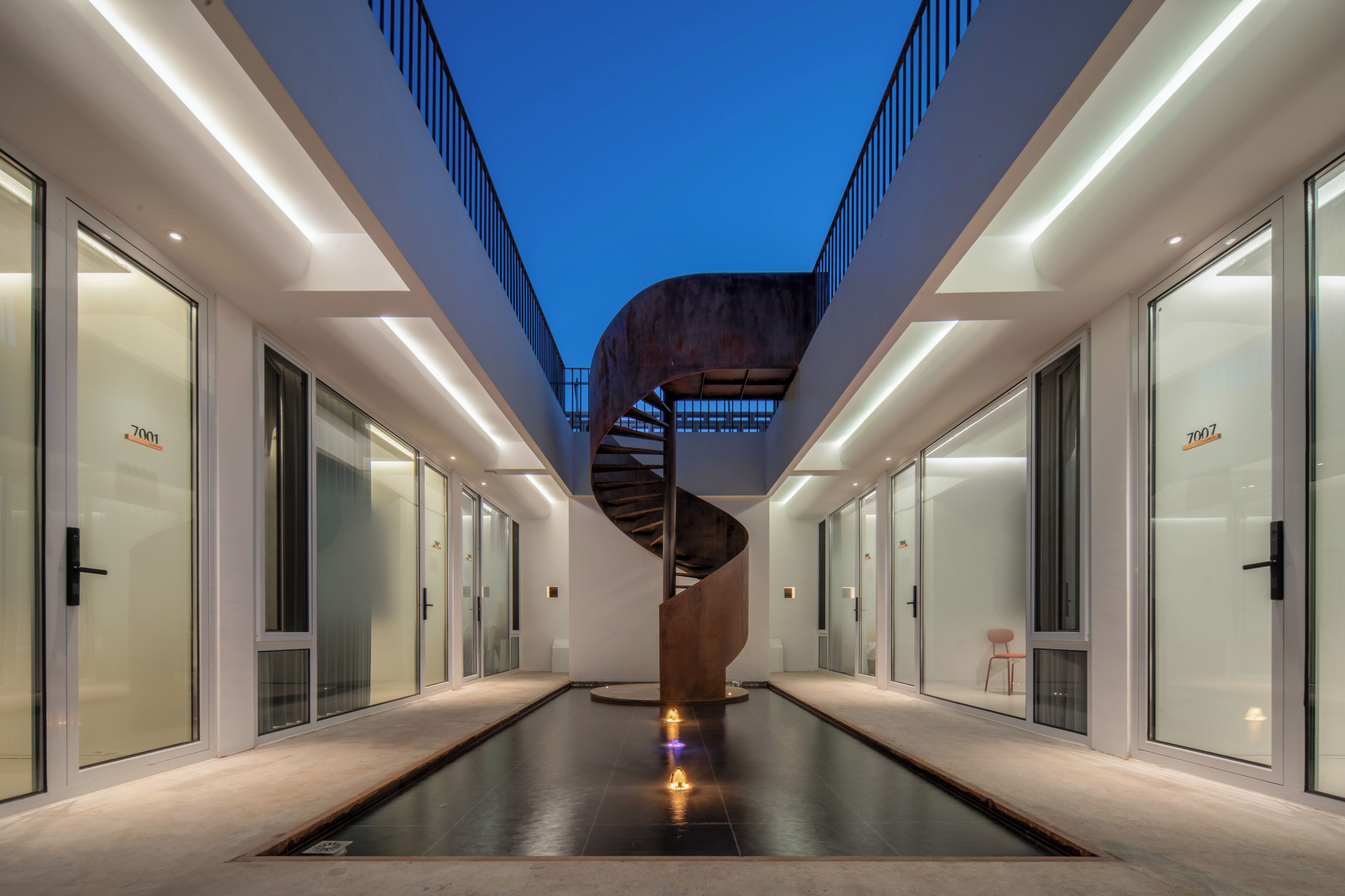 Un edificio moderno con una escalera espiral central, puertas de cristal y una piscina.