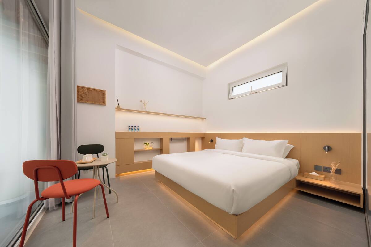 A modern hotel room with a bed, a desk, a chair, and a small table.