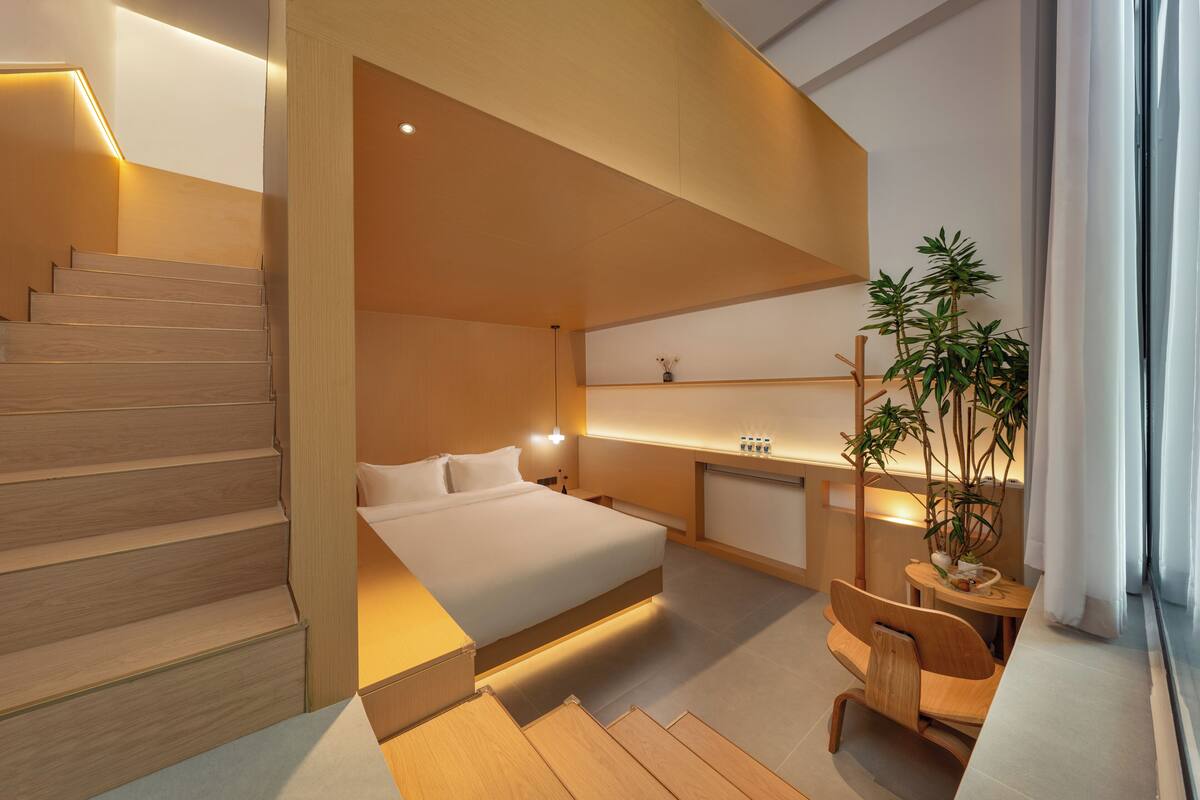 A modern bedroom with a bed, bedside table, lamp, and a staircase.