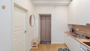 A modern kitchen with white cabinets, a wooden door, a small stool, and a kettle on the counter.