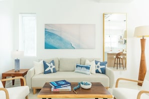 A modern living room with a sofa, a coffee table with books, a bowl of fruit, and a painting on the wall. - NEW Luxury Grace Bay villa,Pool,2 min>Beach&Reef (The Bight Settlement)