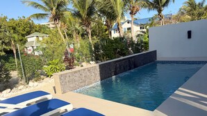 En swimmingpool med blå solstolar, omgiven av grönska och en vit byggnad.