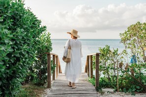Ein hölzerner Weg führt zu einem Strand, flankiert von viel Grün.