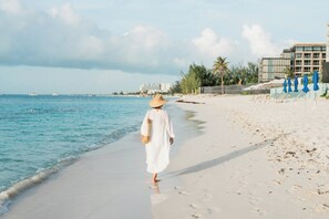 A beach with a person walking along the shore, a building in the background, and a clear sky. - NEW Luxury Grace Bay villa,Pool,2 min>Beach&Reef (The Bight Settlement)