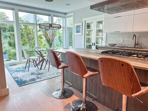 Une cuisine moderne dotée d’un grand îlot central, de tabourets de bar et offrant une vue sur la verdure environnante.