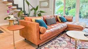 Een moderne woonkamer met een leren bank, een ronde salontafel, een klein bijzettafeltje en een trap.