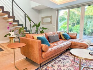 Un salon moderne avec un canapé en cuir, une table basse ronde, une petite table d’appoint et un escalier.