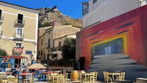 Una calle con terrazas al aire libre, edificios y una montaña al fondo.