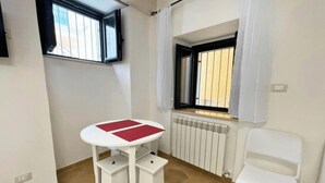 Una habitación pequeña con una mesa y una silla blancas, un radiador y una ventana con cortinas.