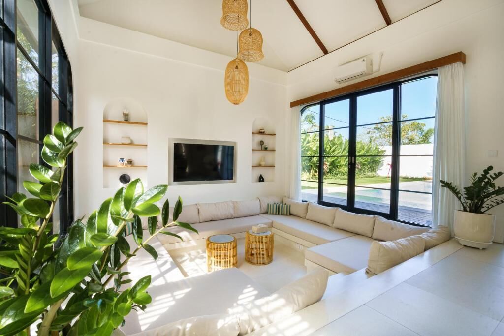 A spacious living room with a large sectional sofa, a flat-screen TV, and a large window offering a view of greenery.