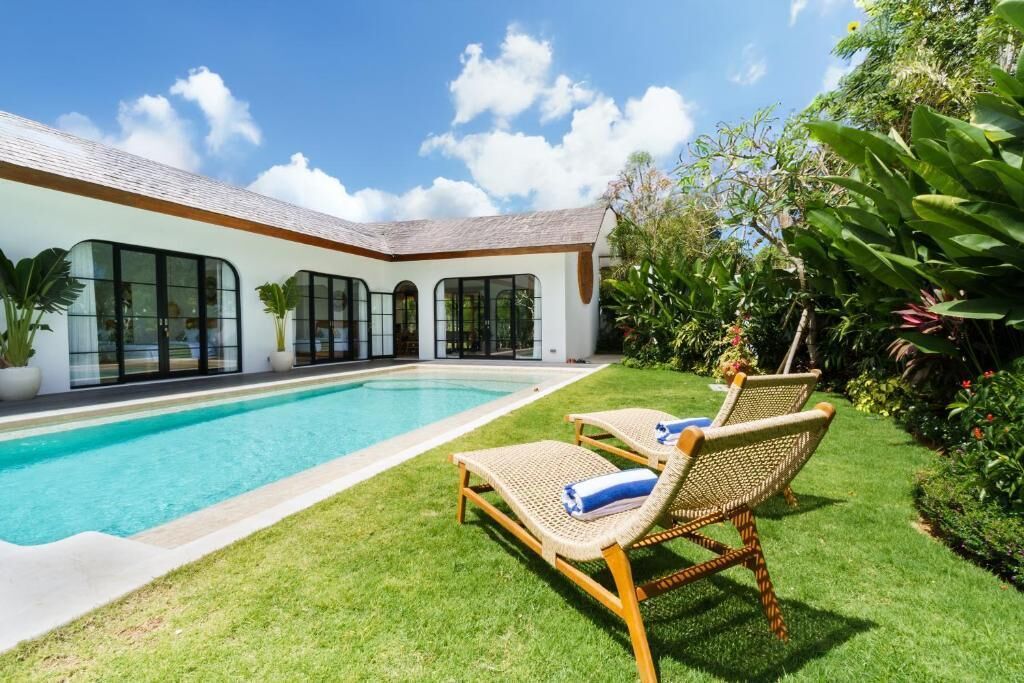 A modern house with a swimming pool, two wicker lounge chairs, and a well-maintained garden.