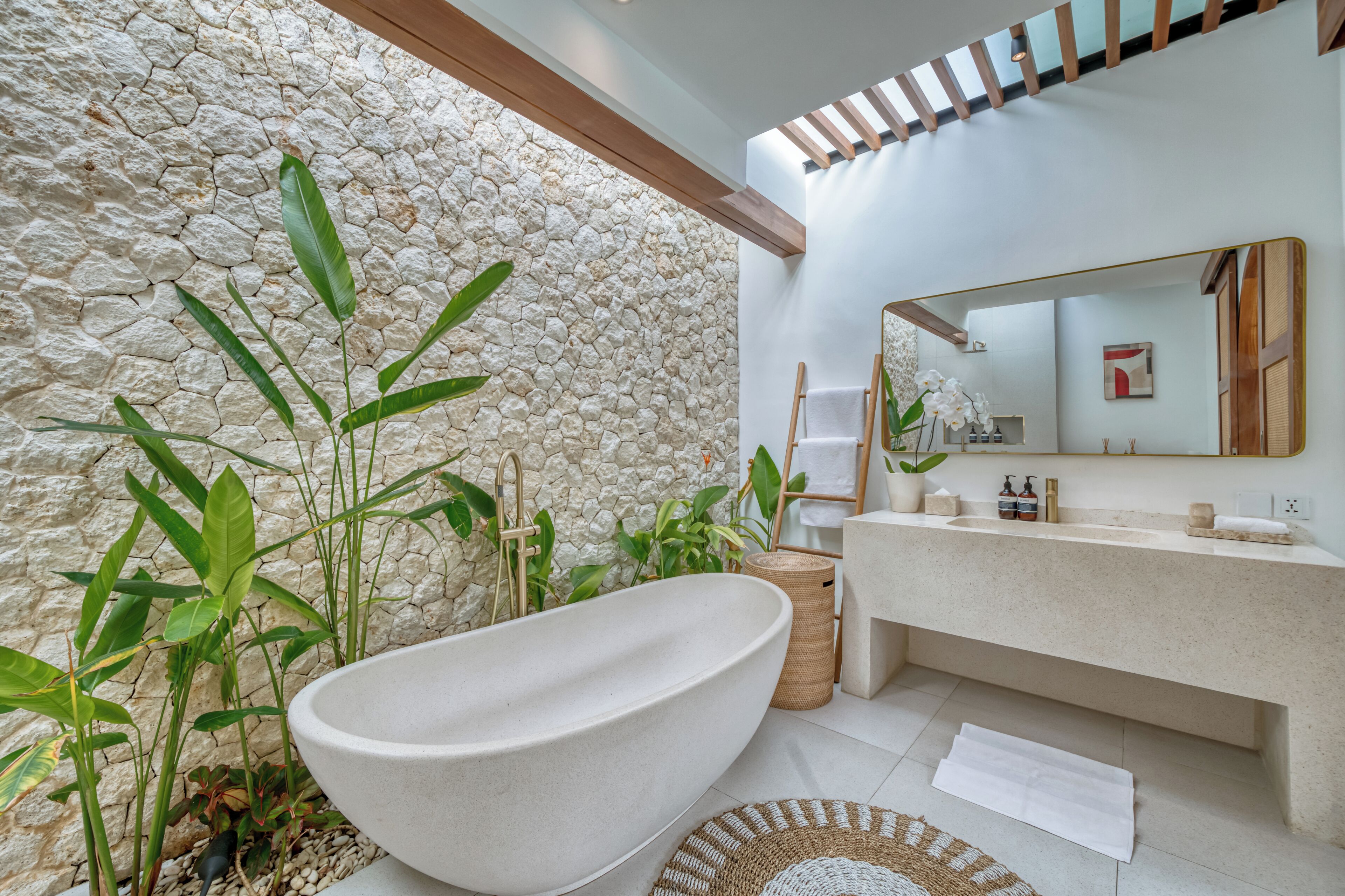 A modern bathroom with a freestanding bathtub, a stone wall, and a large mirror.