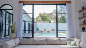 A modern living room with a large sliding glass door leading to a pool area. - Villa Yasmine Althea by Senada (Pecatu)