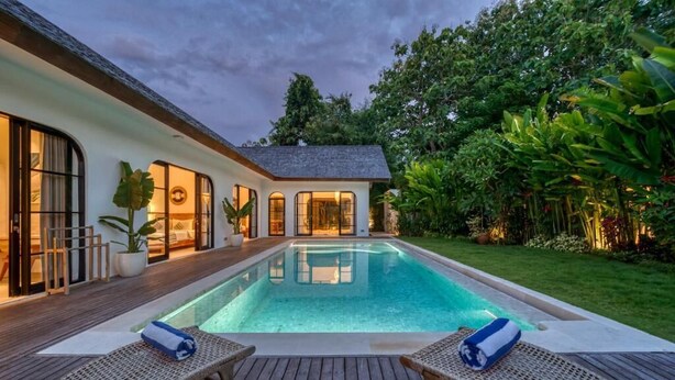 A swimming pool with lounge chairs, a wooden deck, and a house with large windows. - Villa Yasmine Althea by Senada (Pecatu)
