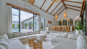 A spacious living area with a large window, a dining set, and a staircase leading to an upper level. - Villa Yasmine Althea by Senada (Pecatu)