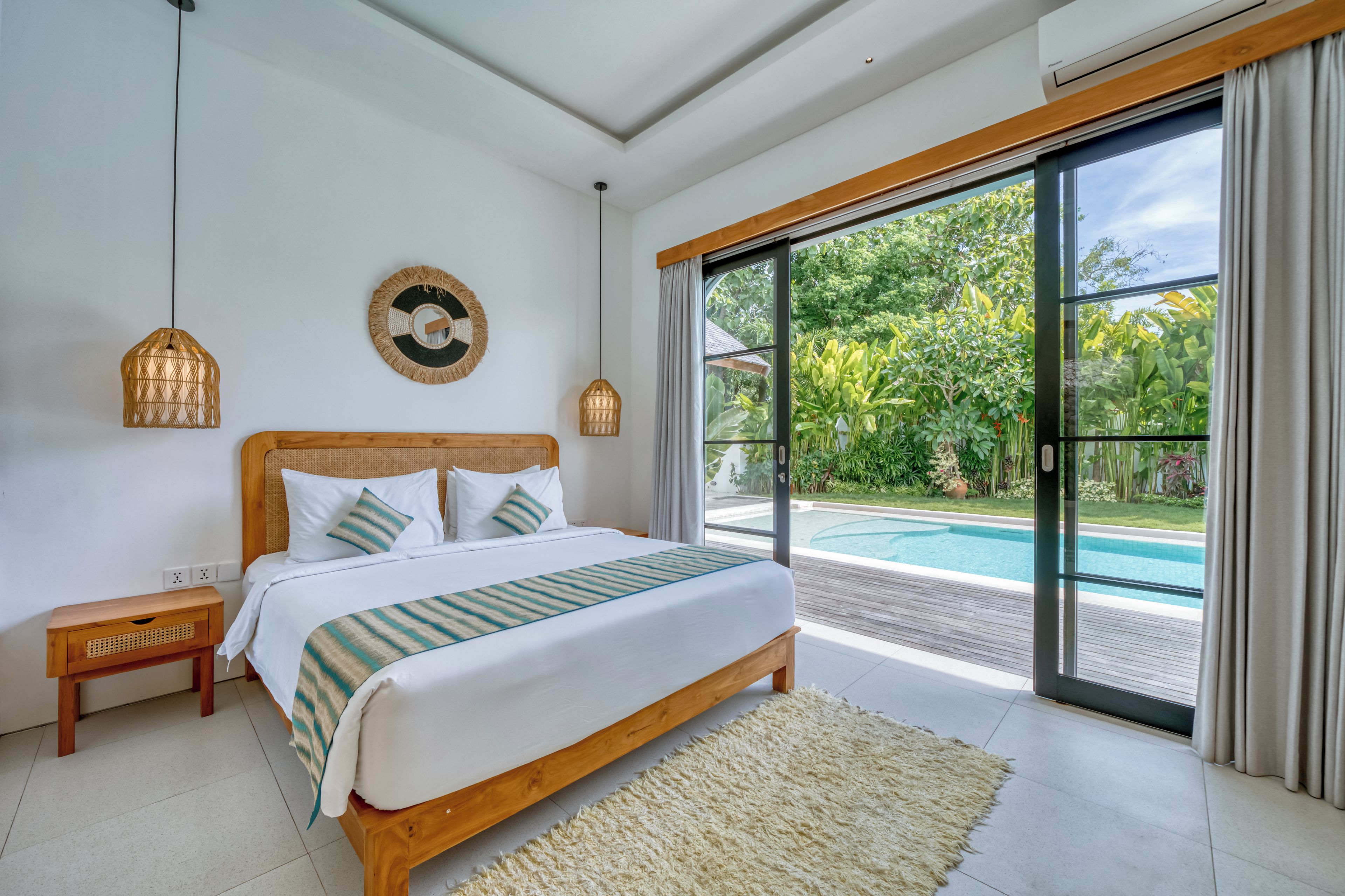 Une chambre dotée d’un grand lit, d’une table de chevet, d’une lampe fixée au mur et offrant une vue sur une piscine grâce à une porte-fenêtre coulissante.