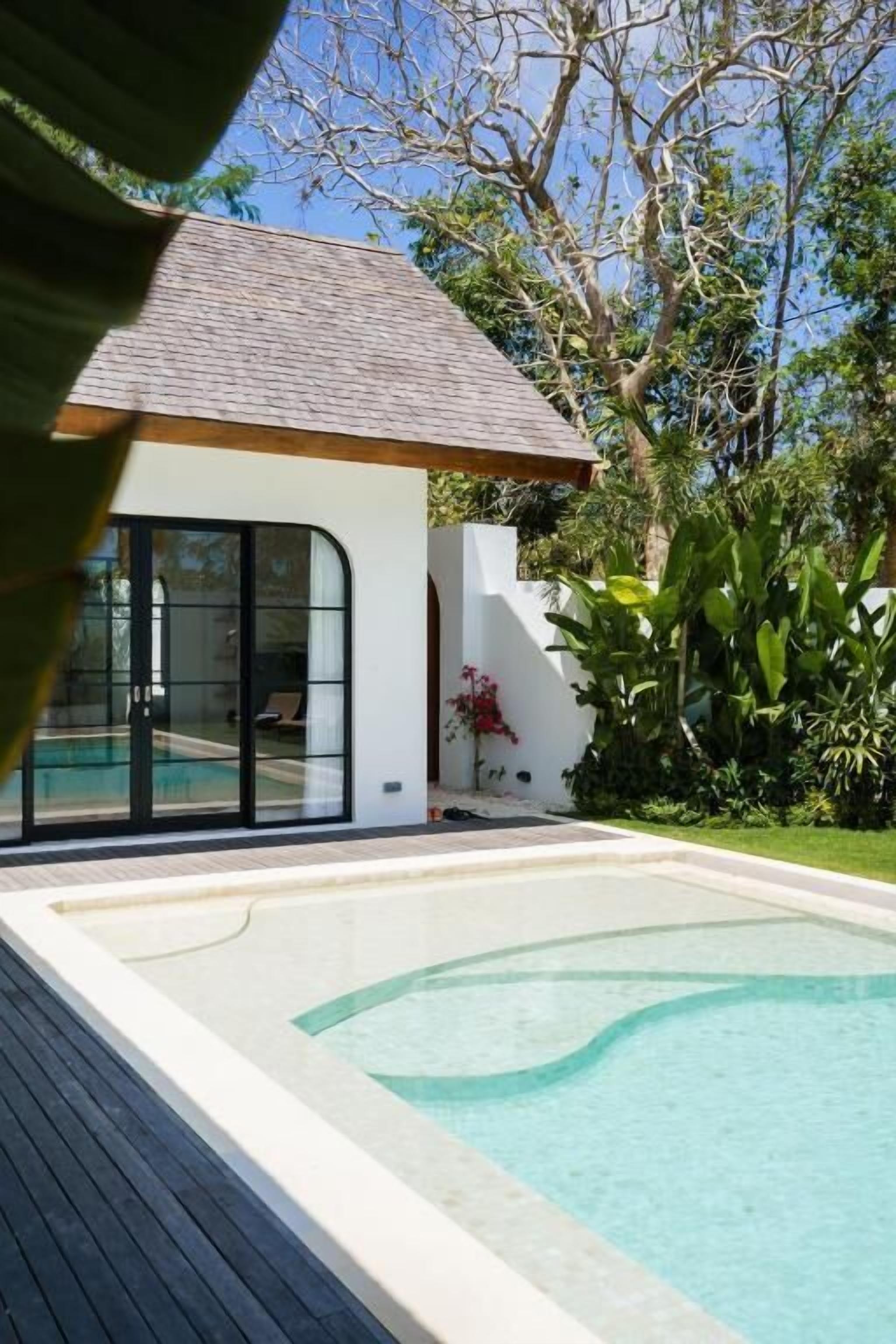 Ein modernes Haus mit Schwimmbad, einer überdachten Terrasse und üppiger Bepflanzung.
