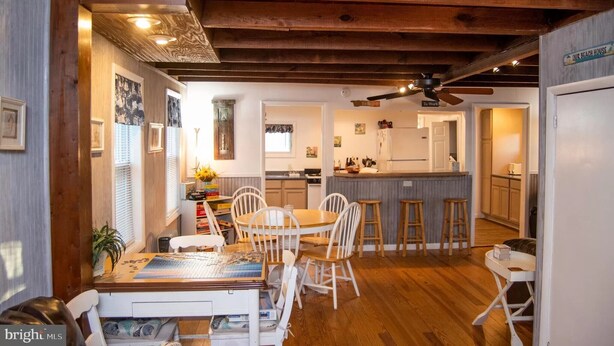 Una cocina con vigas de madera, una zona de comedor con una mesa y sillas, y una barra con taburetes.