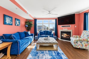 Ein Wohnzimmer mit Kamin, zwei blaue Sofas, einem bunten Sessel und einem großen Fenster.