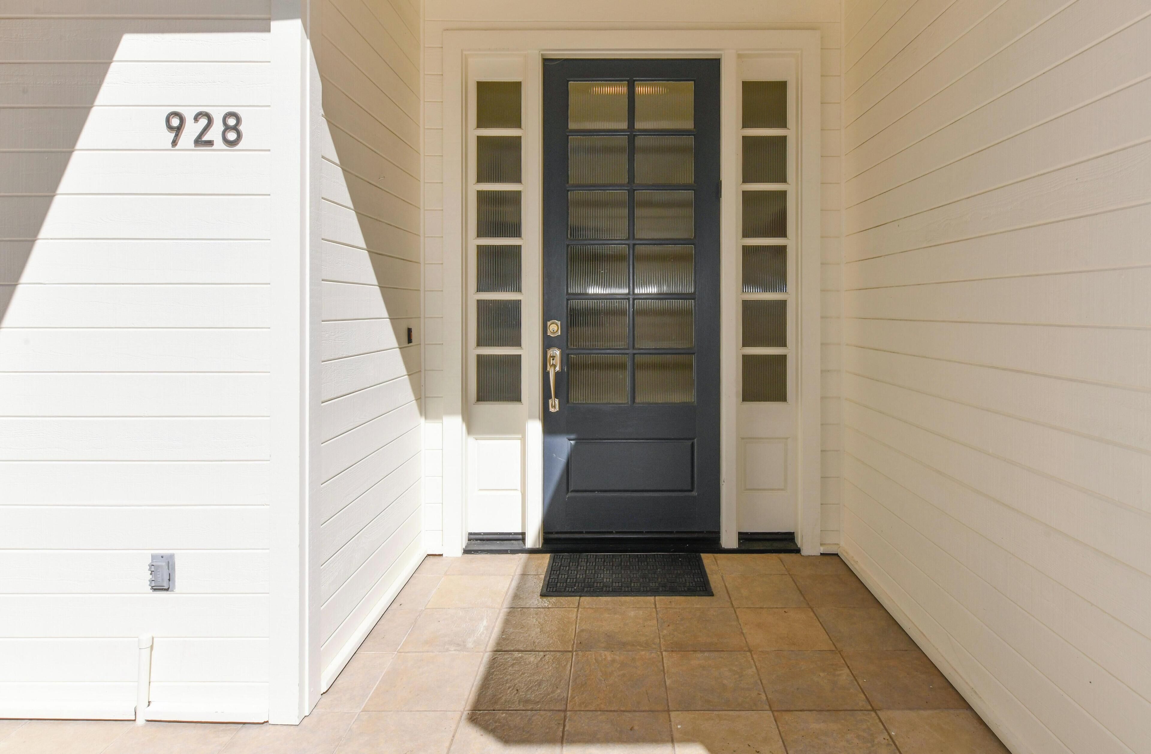 A front door with a number '928' above it, a dark-colored door with glass panels, and a black doormat on a tiled floor.