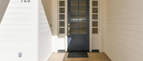 A front door with a number '928' above it, a dark-colored door with glass panels, and a black doormat on a tiled floor.