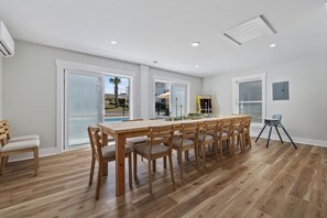 Uma área de refeições com mesa e cadeiras de madeira, janelas amplas e vista para o exterior.