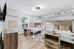 Quarto com beliches, escrivaninha, televisão e tapete estampado.