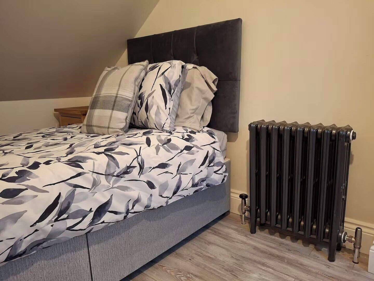 A bedroom with a bed, a radiator, and a wooden floor.