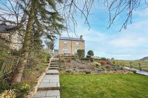 A stone staircase leading to a two-story house with a garden and a view of the countryside.