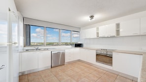 A modern kitchen with white cabinets, a stainless steel dishwasher, an oven, and a microwave. - Gemini Resort 55 Stunning Ocean Views (Golden Beach)
