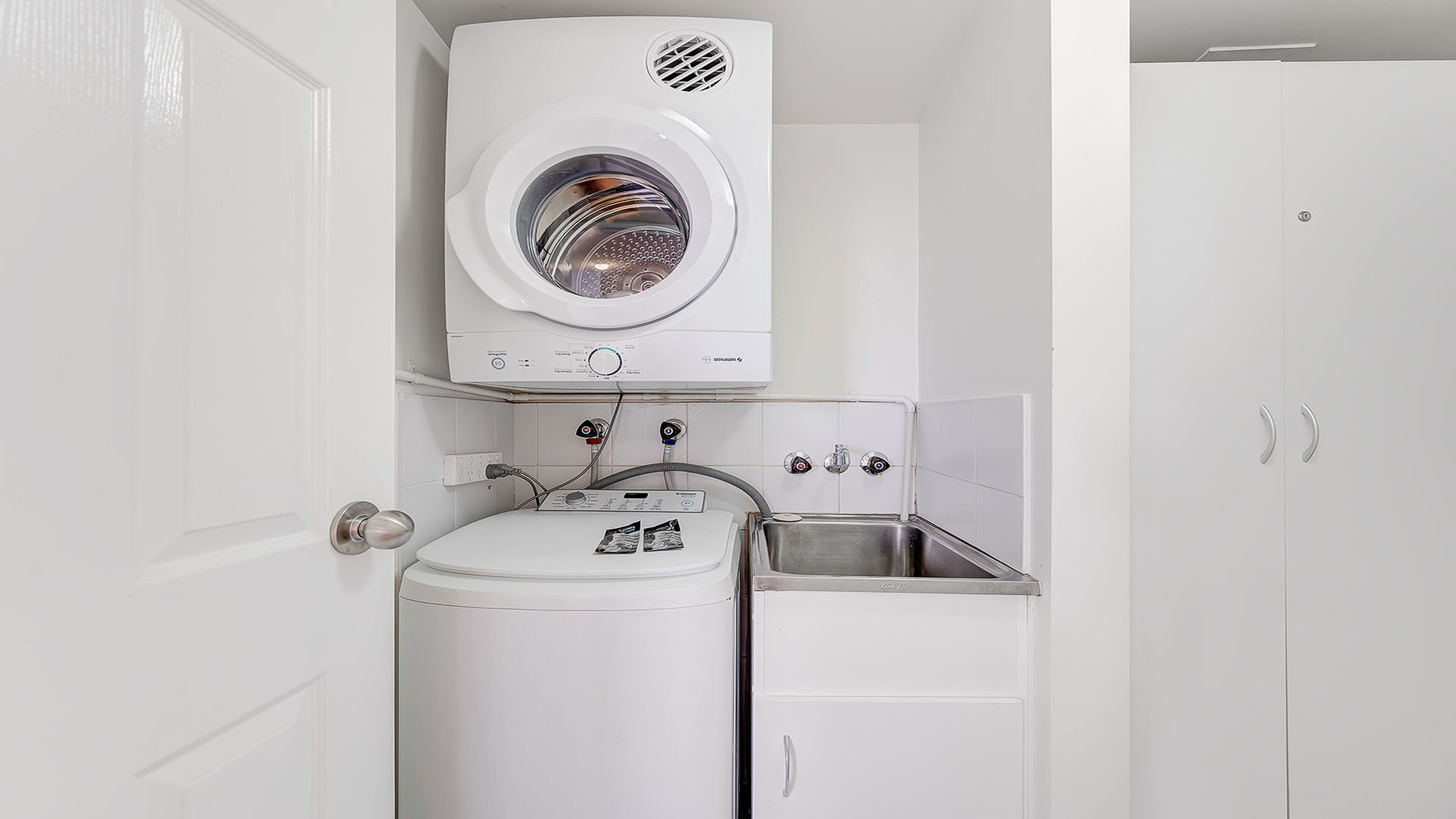 A compact laundry room with a front-loading washing machine, a dryer, and a sink.