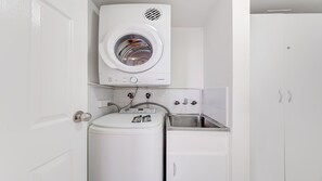 Ein kleiner Hauswirtschaftsraum mit einer Waschmaschine mit Frontlader, einem Trockner und einem Waschbecken.