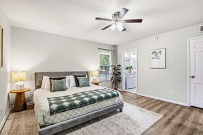 Ein Schlafzimmer mit Bett, Nachttischen, Deckenventilator, Fenster und Tür.